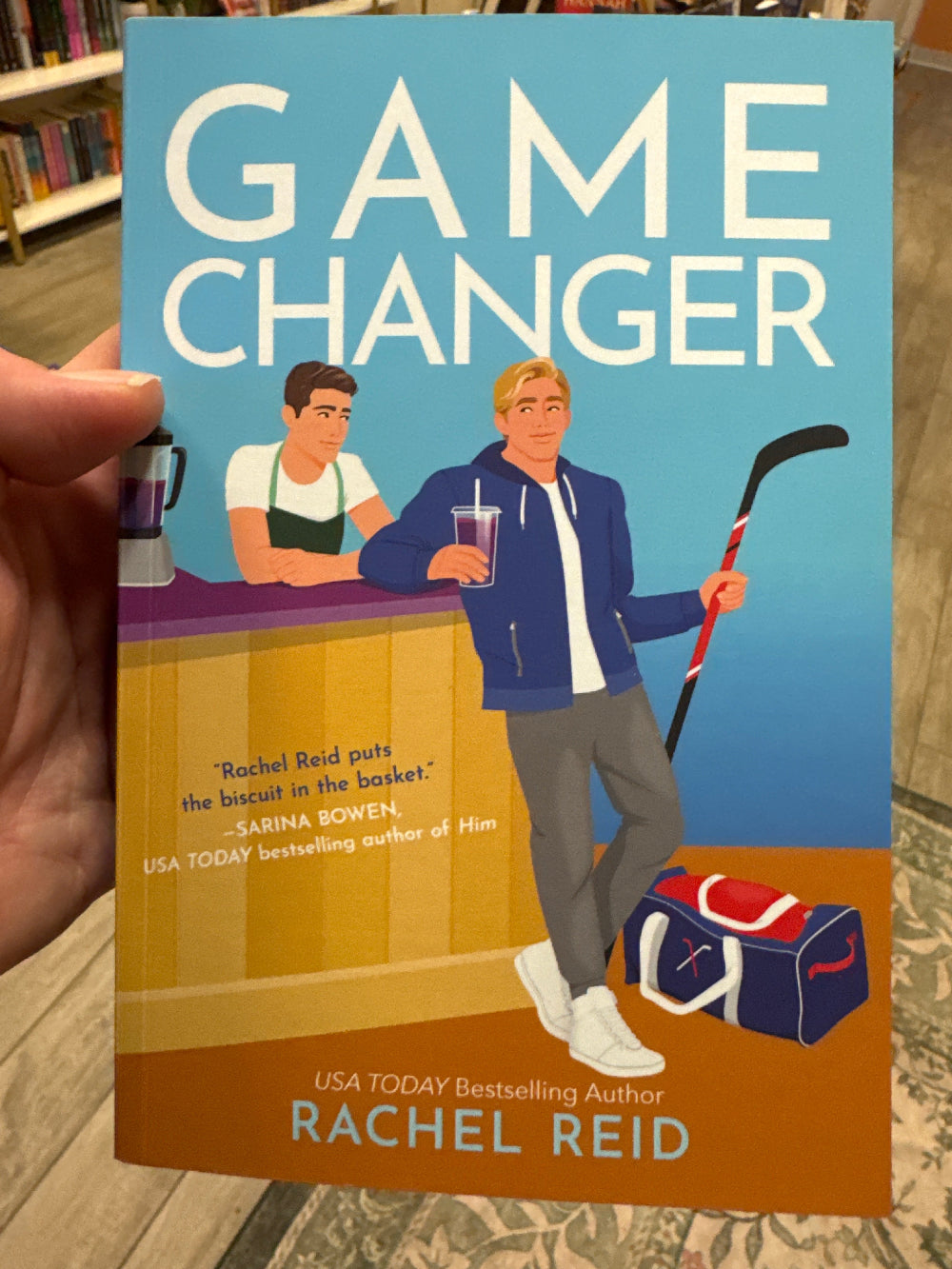 Book titled 'Game Changer' by Rachel Reid held in a hand with a patterned background.