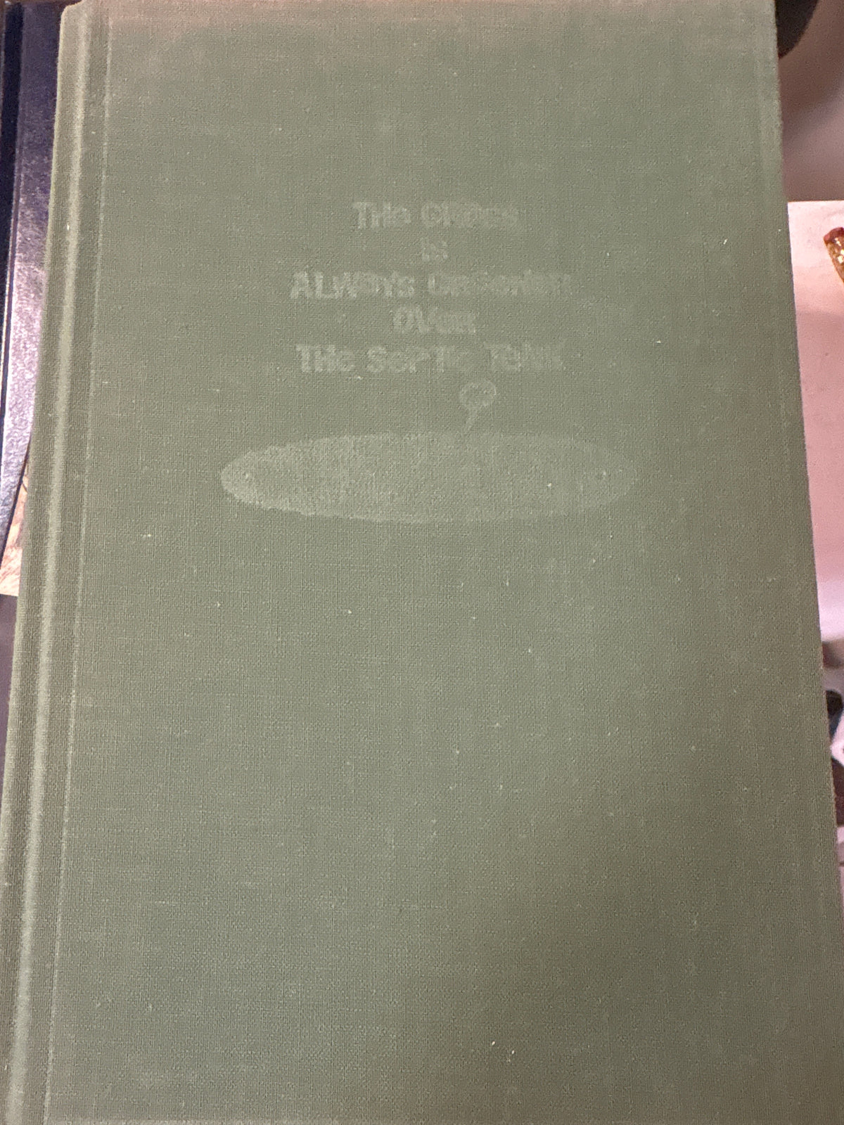 Sage green cloth-bound hardcover book 'The Grass is Always Greener Over the Septic Tank' with embossed mushroom cover design