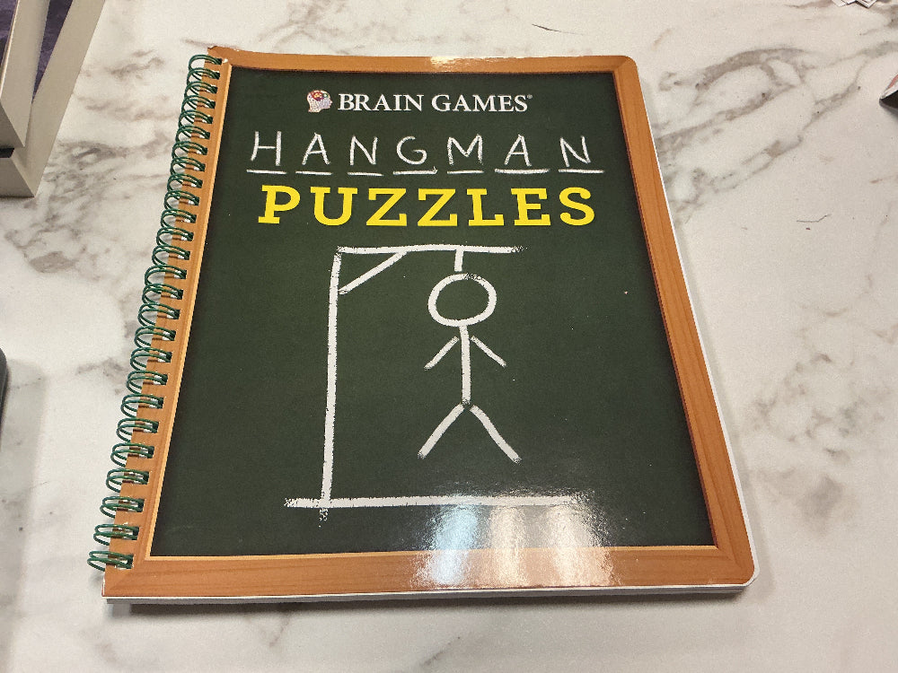 Book titled 'Hangman Puzzles' by Brain Games on a marble surface