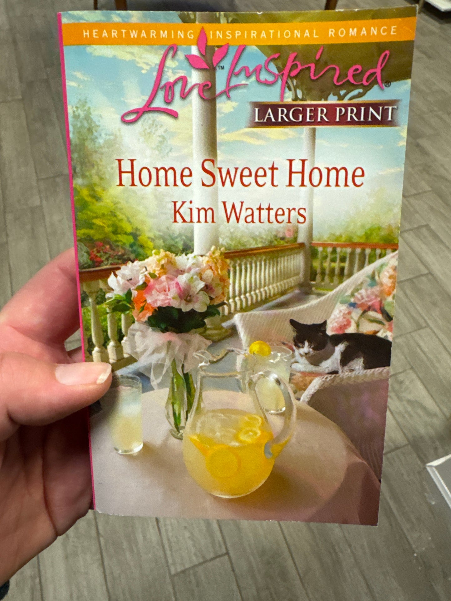 Book titled 'Home Sweet Home' by Kim Watters held by a hand on a wooden floor.