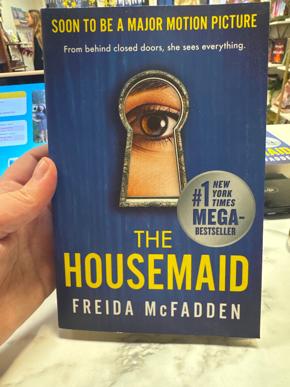 Book titled 'The Housemaid' by Freida McFadden held in a hand with a blurred background