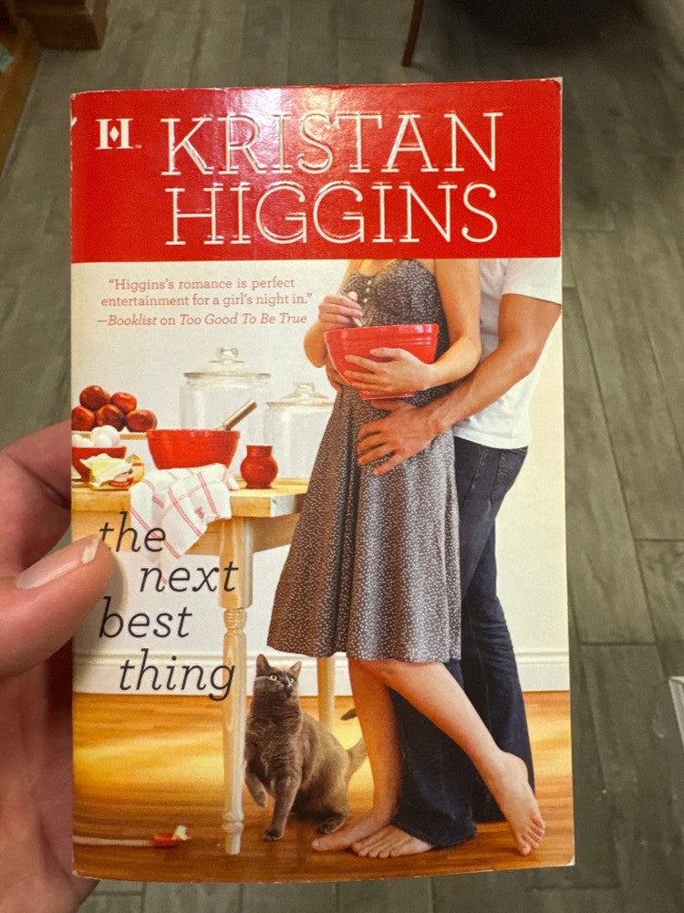Book titled 'The Next Best Thing' by Kristan Higgins held in a hand with a blurred background.