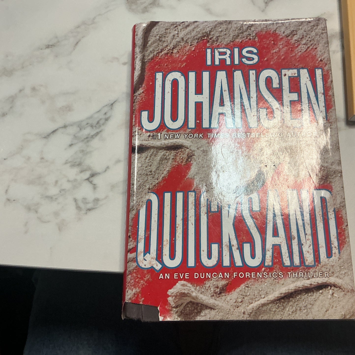 Book titled 'Quicksand' by Iris Johansen on a marble surface