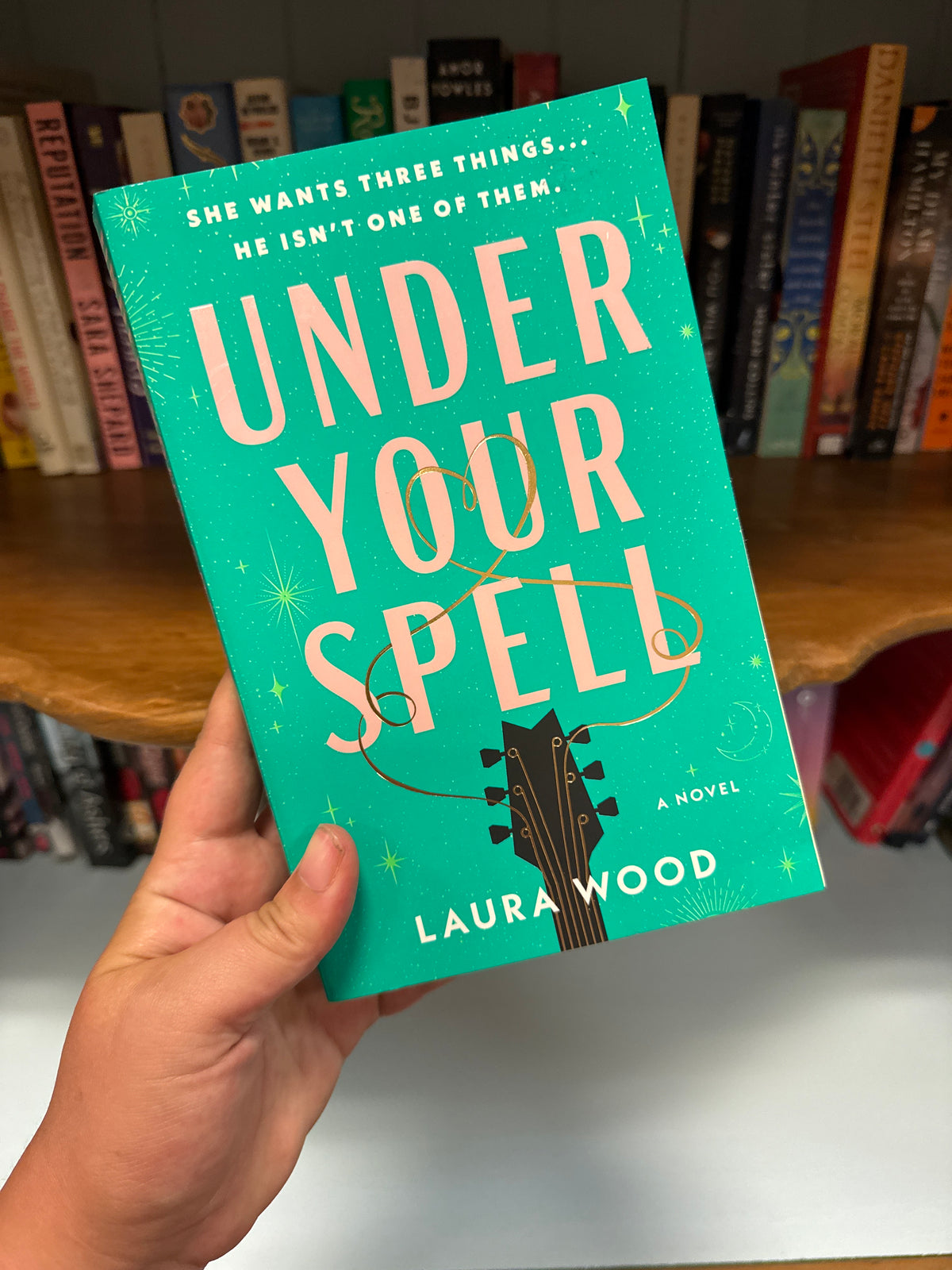 Under Your Spell teal hardcover novel by Laura Wood with gold heart string detail