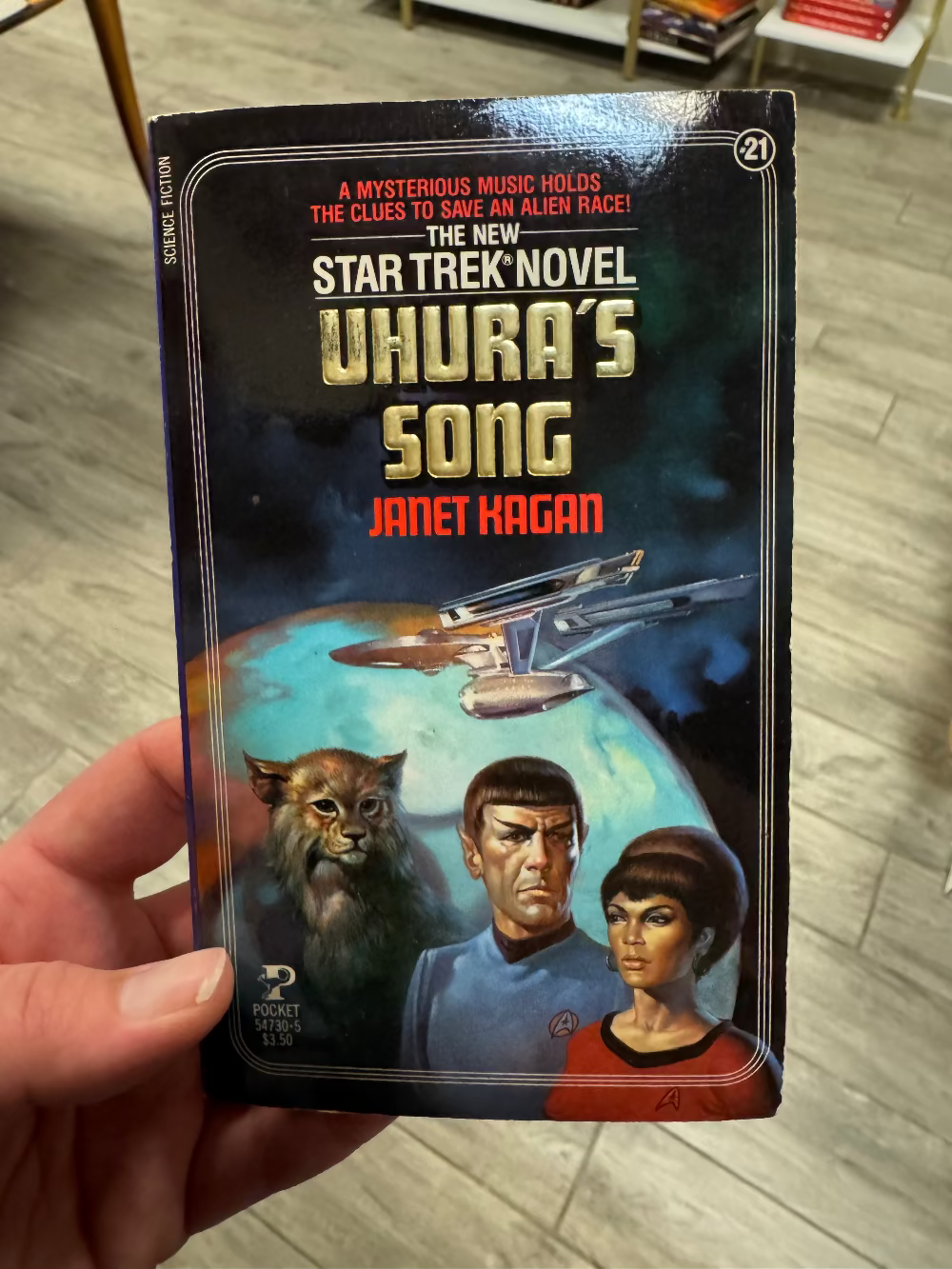 Book titled 'Uhura's Song' by Janet Kagan held in a hand on a wooden floor.