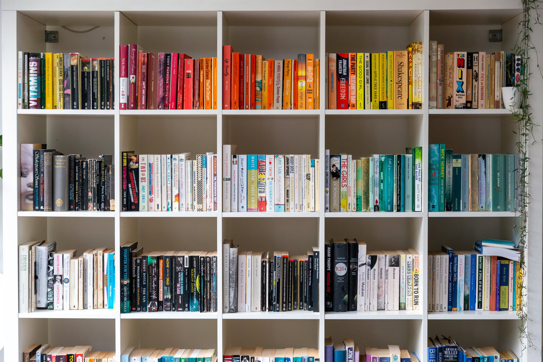 White shelves with books that are red, orange, yellow, green, blue, white, and black