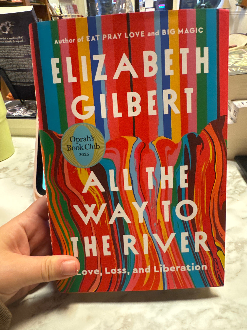 Book titled 'All the Way to the River' by Elizabeth Gilbert held by a person.