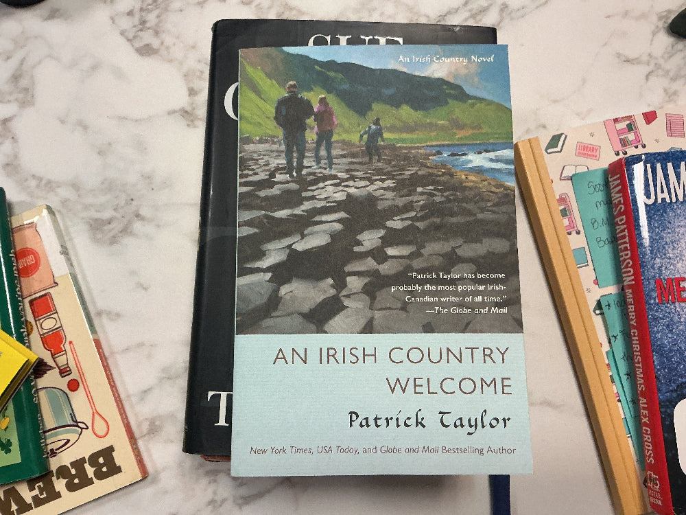 Book titled 'An Irish Country Welcome' by Patrick Taylor on a marble surface with other books.