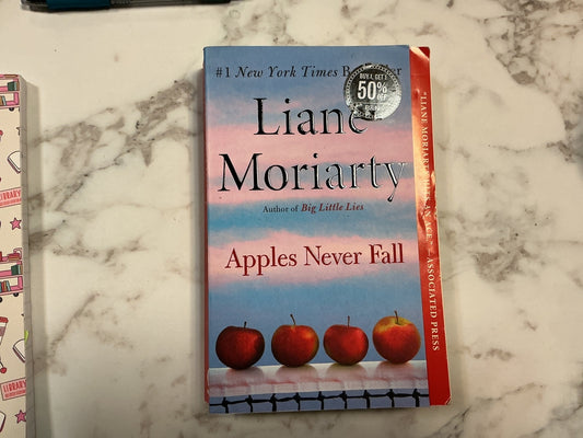 Book titled 'Apples Never Fall' by Liane Moriarty on a marble surface