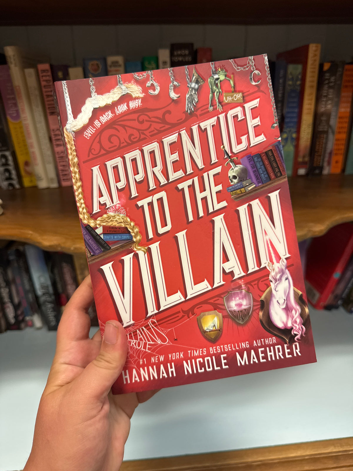 Apprentice to the Villain hardcover book by Hannah Nicole Maehrer with gold rope detailing and unicorn skull cover art