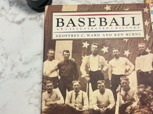 Book titled 'Baseball: An Illustrated History' by Geoffrey C. Ward and Ken Burns on a marble surface.