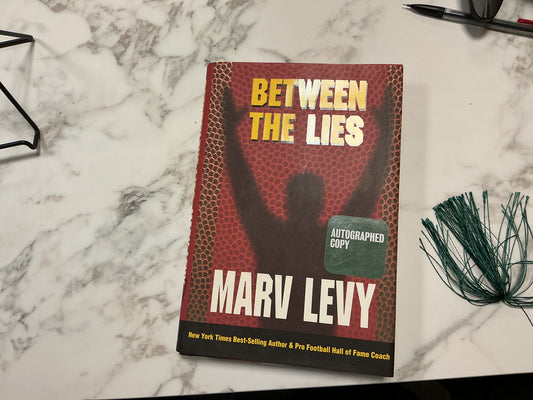 Autographed hardcover Between The Lies by Marv Levy with red honeycomb cover and author silhouette