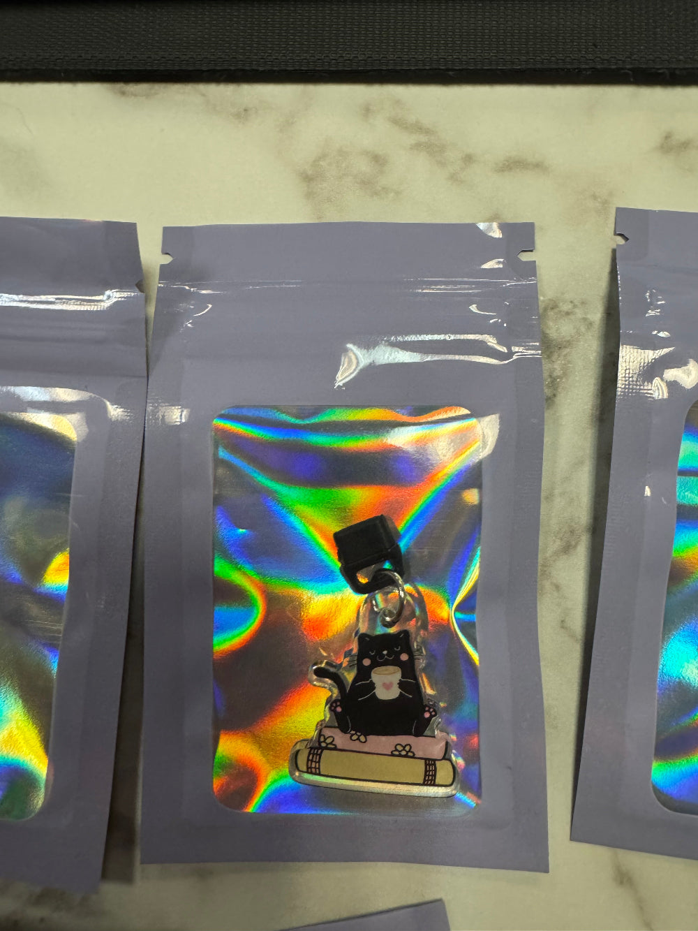 Holographic packaging with black cat inside sitting on books kindle charm in it