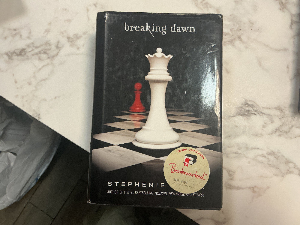 Book titled 'Breaking Dawn' by Stephenie Meyer with a chess piece design on the cover, placed on a marble surface.