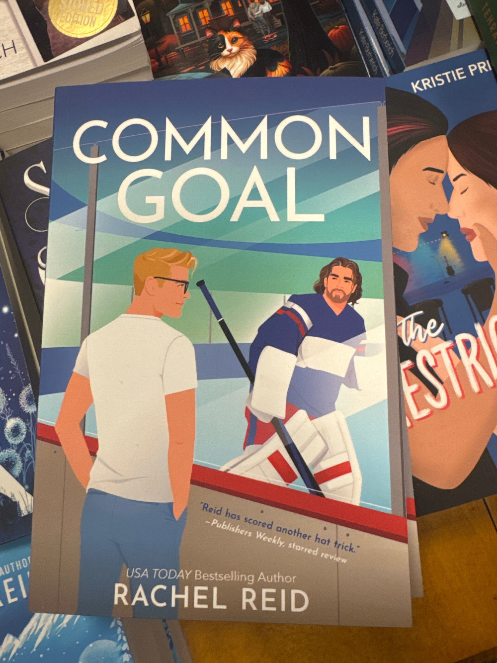 Book titled 'Common Goal' by Rachel Reid on a stack of other books.