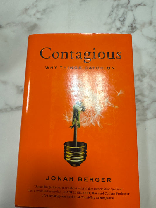 Contagious hardcover book by Jonah Berger with orange cover and dandelion lightbulb illustration