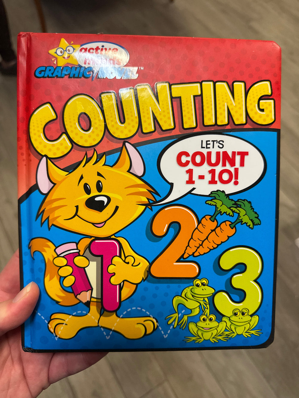 Children's book titled 'Counting' held by a hand on a wooden surface