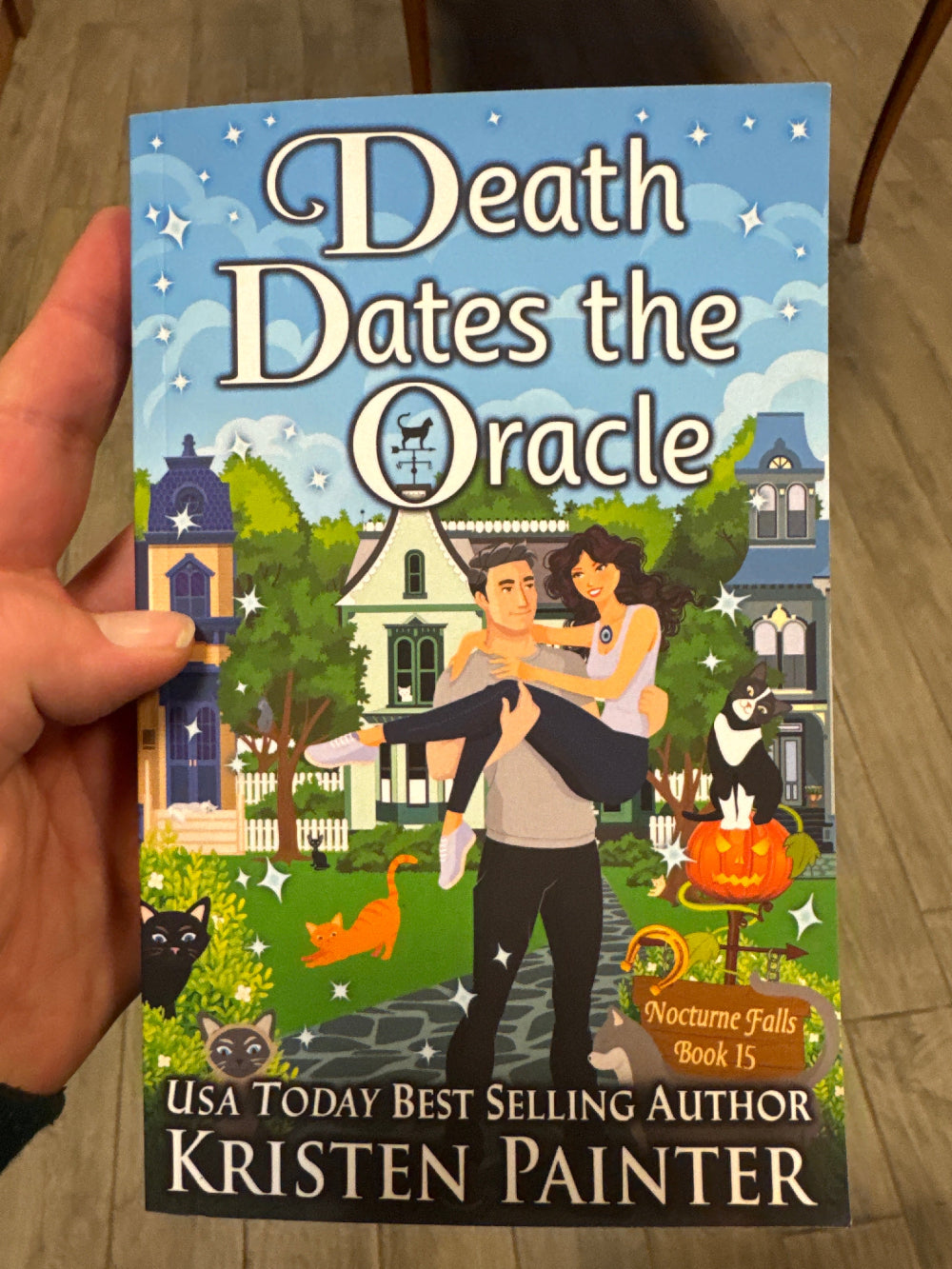 Book titled 'Death Dates the Oracle' by Kristen Painter held in a hand.