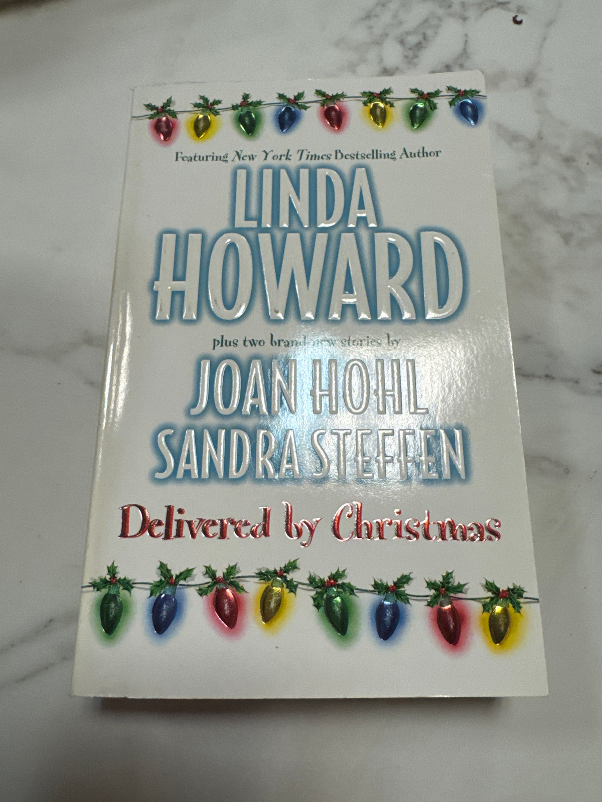 Delivered by Christmas paperback book with red metallic script and holly decoration