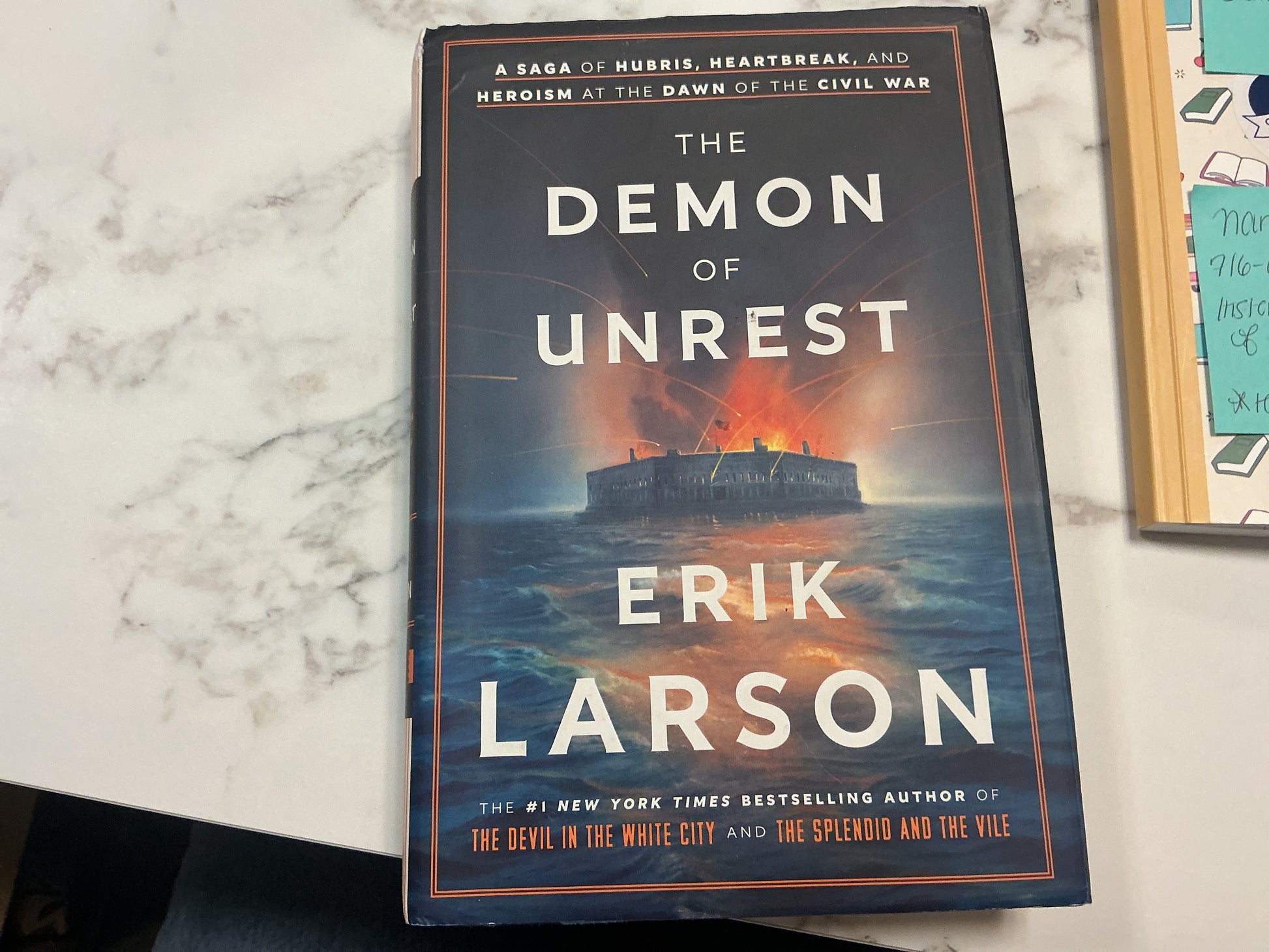 Book titled 'The Demon of Unrest' by Erik Larson on a marble surface