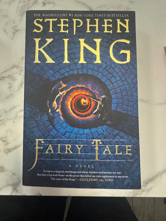 Stephen King's 'Fairy Tale' novel book cover, featuring a dark blue background with a glowing orange spiral and gold lettering, photographed on a white marble surface.