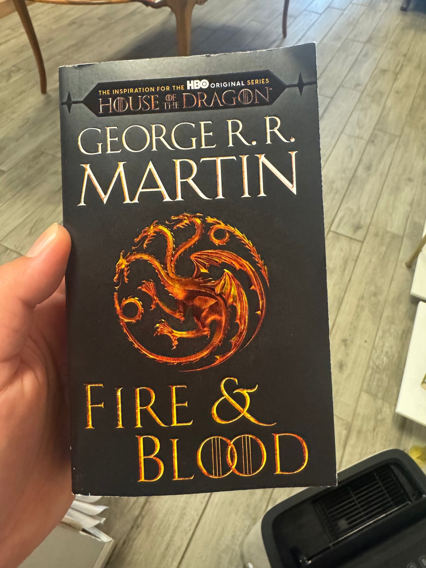 A hand holding a paperback copy of George R.R.