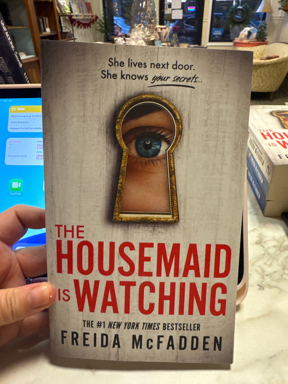 Book titled 'The Housemaid is Watching' held by a person in a store setting.