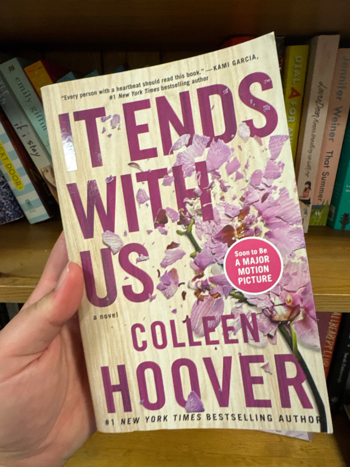 It Ends With Us paperback by Colleen Hoover with purple title and flower petals