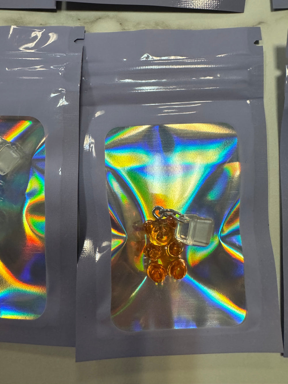 Holographic packaging with Orange Gummy Bear Kindle Charm inside