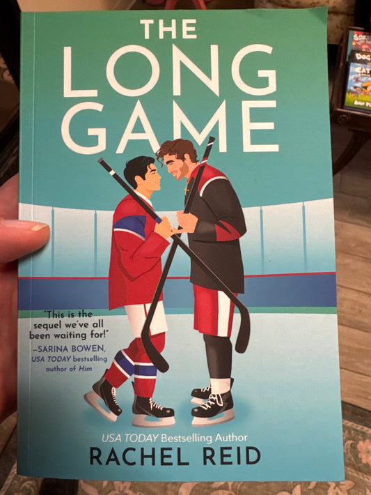Book cover of 'The Long Game' by Rachel Reid held in a hand.
