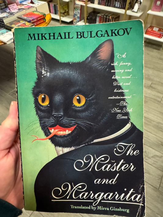 Book cover of 'The Master and Margarita' by Mikhail Bulgakov with a black cat illustration, held in a bookstore.