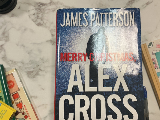 Book titled 'Merry Christmas, Alex Cross' by James Patterson on a marble surface with other books and items.