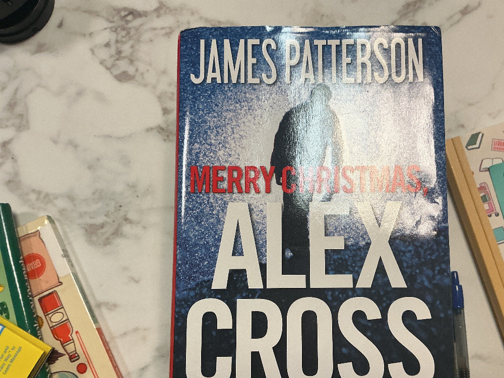 Book titled 'Merry Christmas, Alex Cross' by James Patterson on a marble surface with other books and items.
