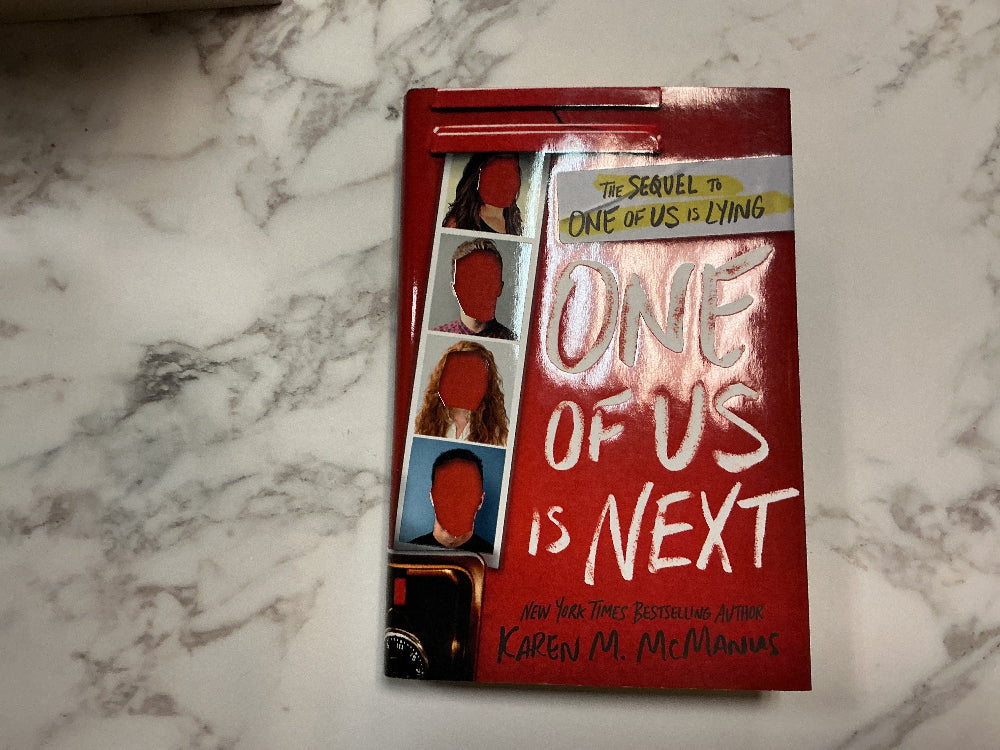 Book titled 'One of Us is Next' on a marble surface