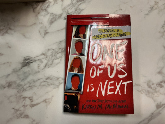 Book titled 'One of Us is Next' on a marble surface