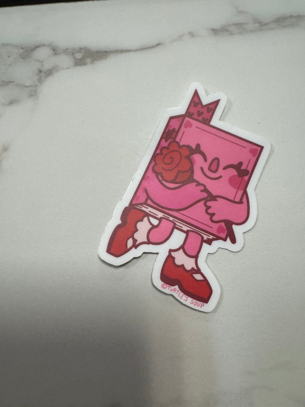 Pink and red sticker with floral design on a light gray background