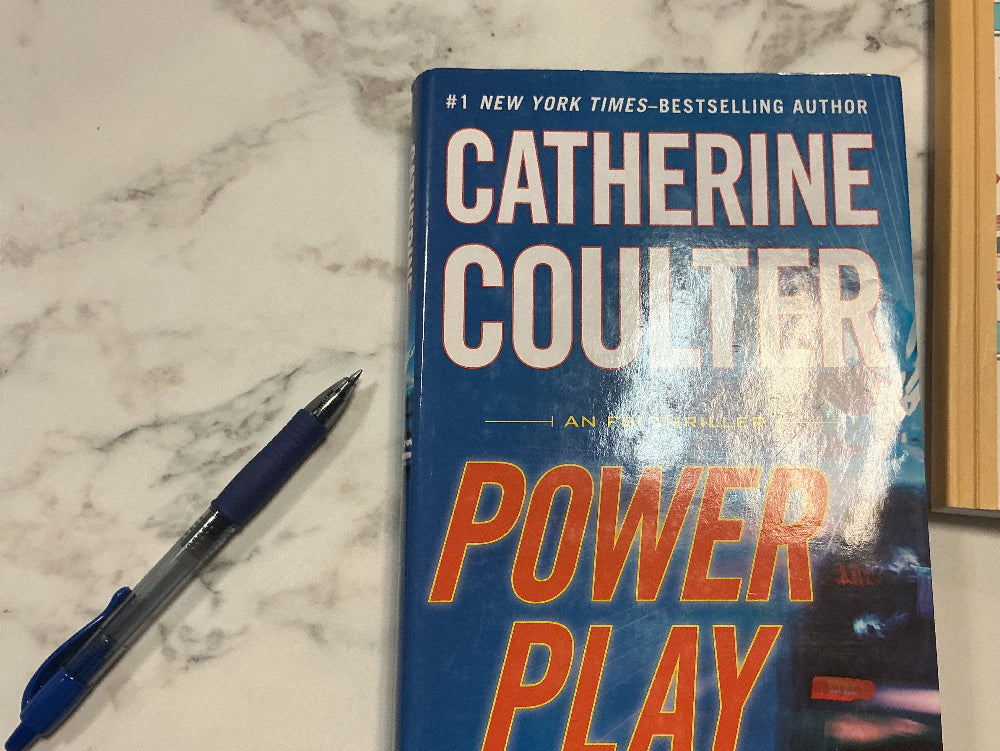 Book titled 'Power Play' by Catherine Coulter on a marble surface with a pen next to it.
