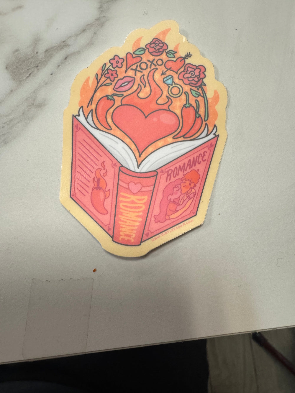 Colorful sticker with a design of a book titled 'Romance' on a white surface.