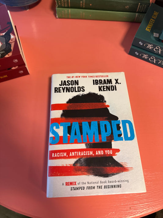 Stamped hardcover book by Jason Reynolds and Ibram X. Kendi on coral table