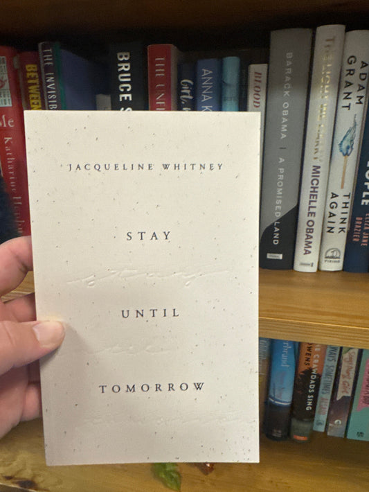 Book titled 'Stay Until Tomorrow' held in front of a shelf with other books.