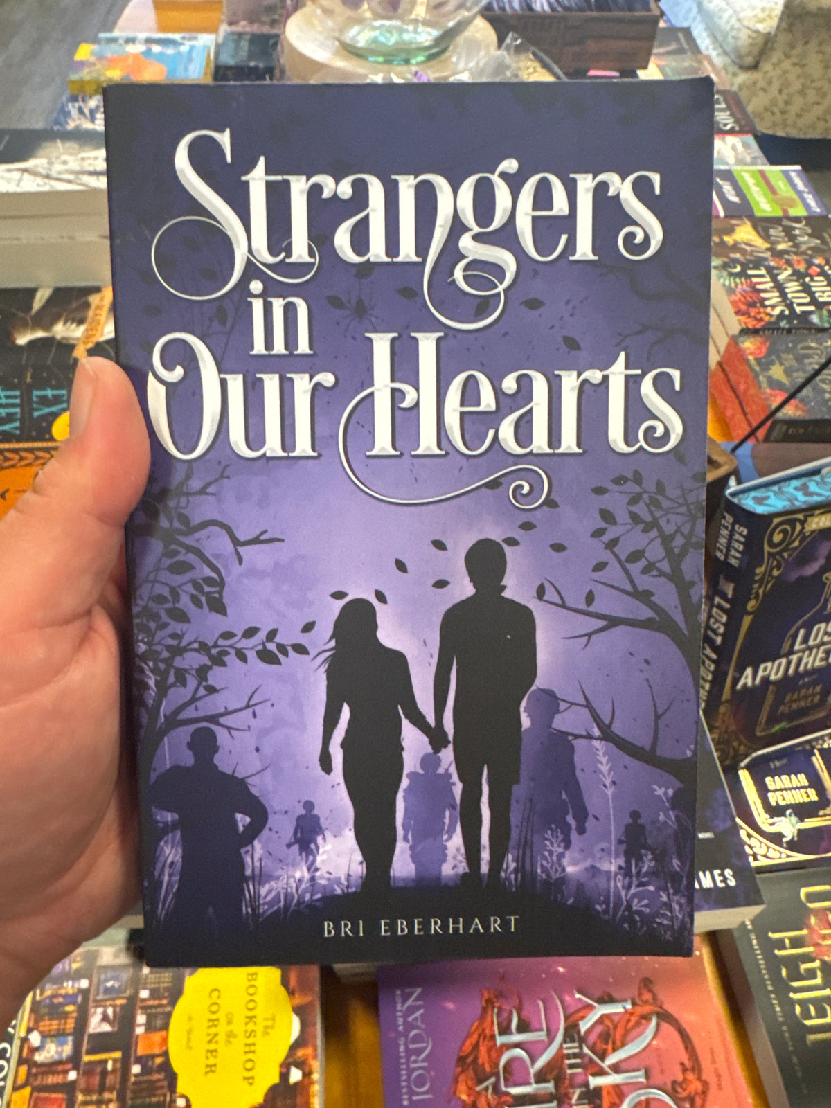 Strangers in Our Hearts paperback book by Bri Eberhart with purple gradient cover and couple silhouettes