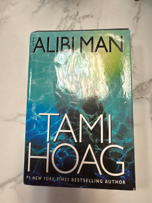 The Alibi Man hardcover book by Tami Hoag with teal and blue underwater cover design