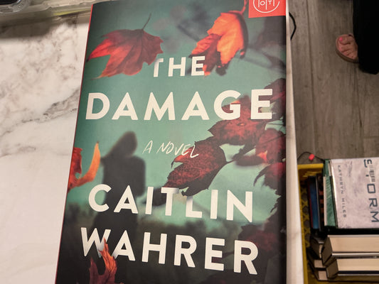 The Damage hardcover novel by Caitlin Wahrer with teal cover and red autumn leaves