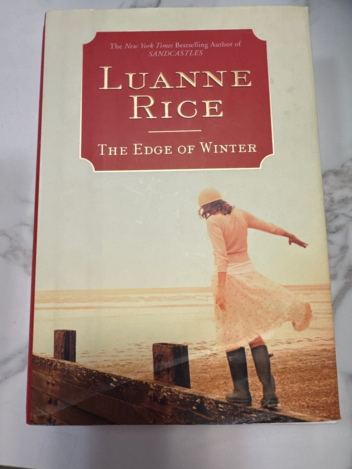 The Edge of Winter hardcover book by Luanne Rice, featuring a cream cover with an illustration of a woman on a beach pier