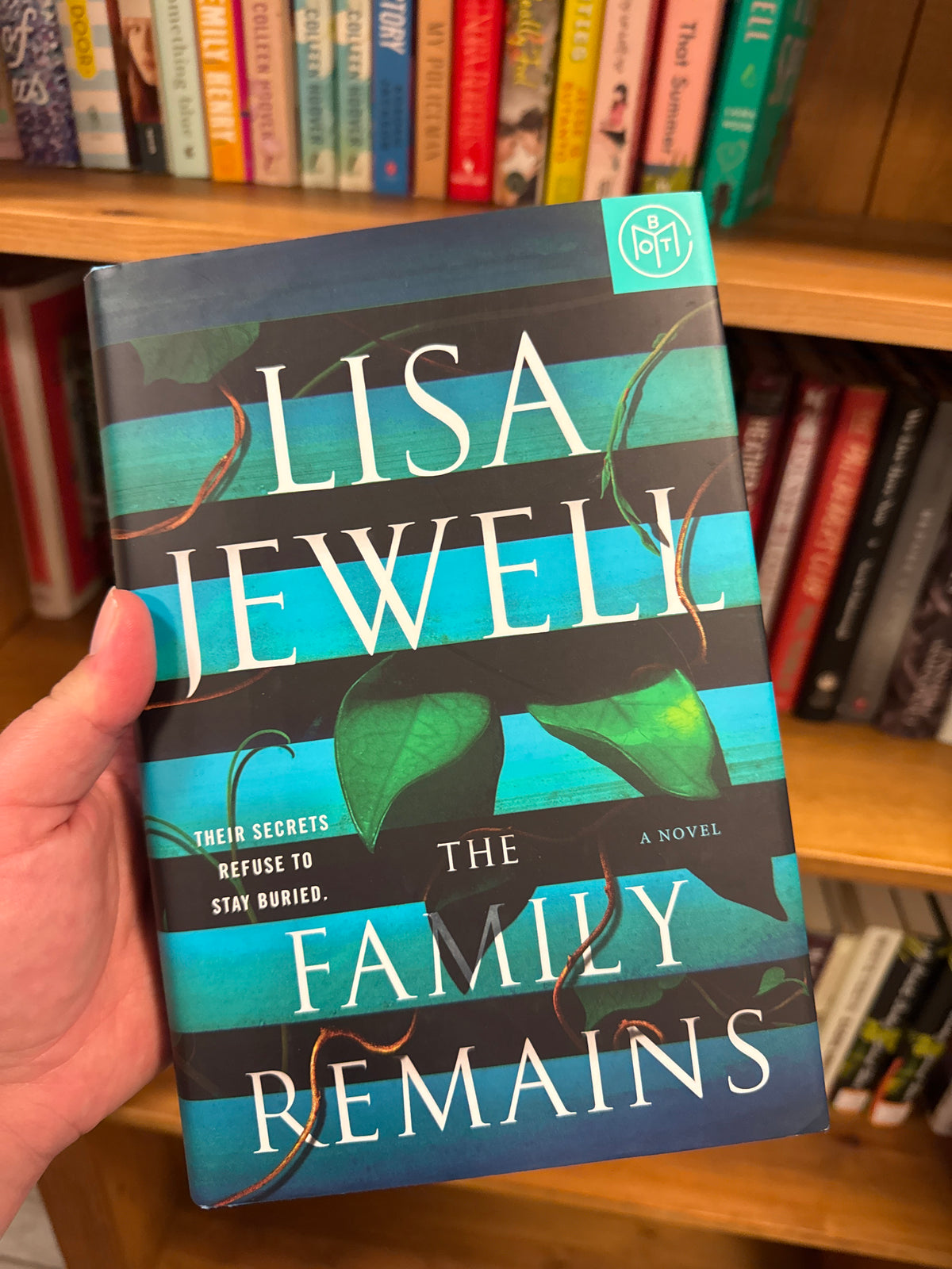 The Family Remains hardcover book by Lisa Jewell with teal and black striped cover