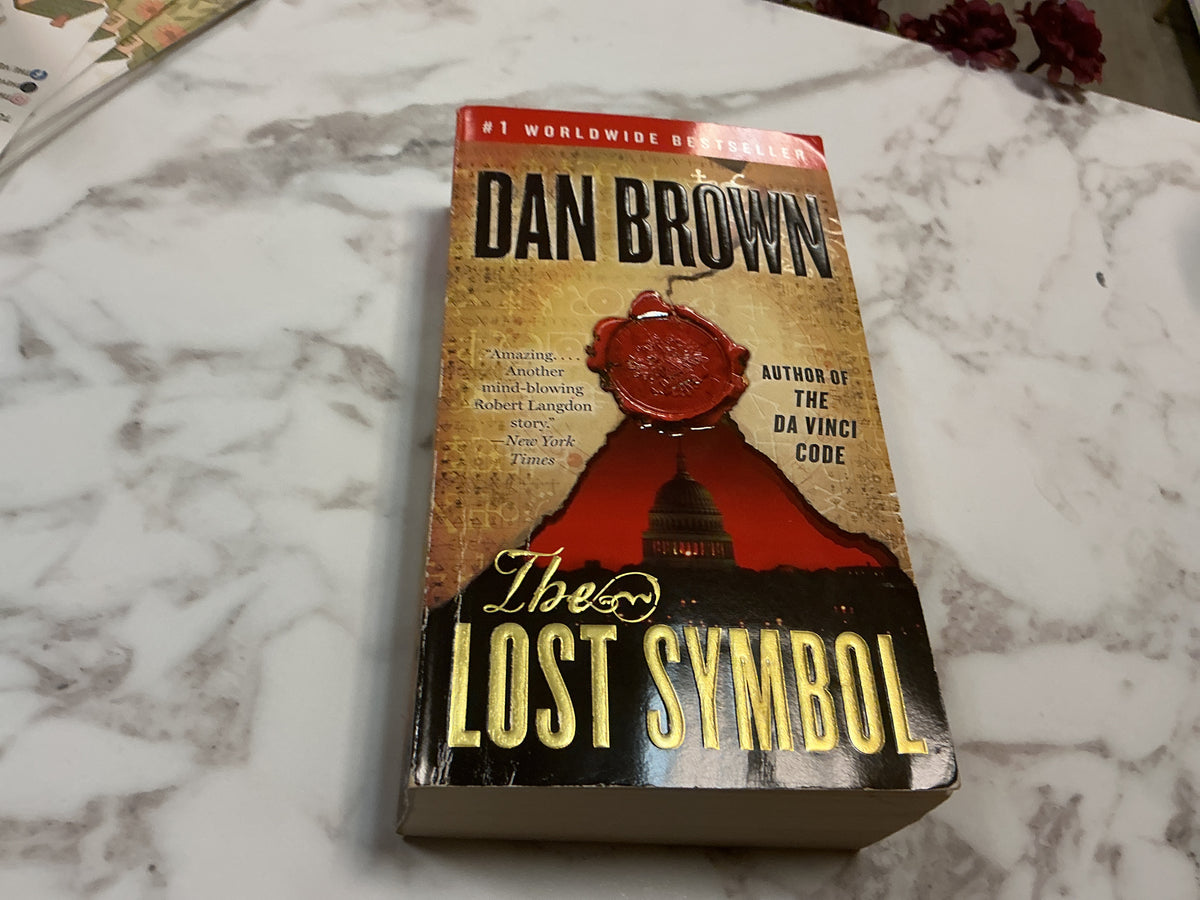 The Lost Symbol paperback by Dan Brown with red wax seal and gold title on white marble
