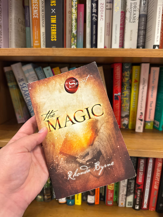 The Magic paperback book by Rhonda Byrne with orange gradient cover and glowing book illustration