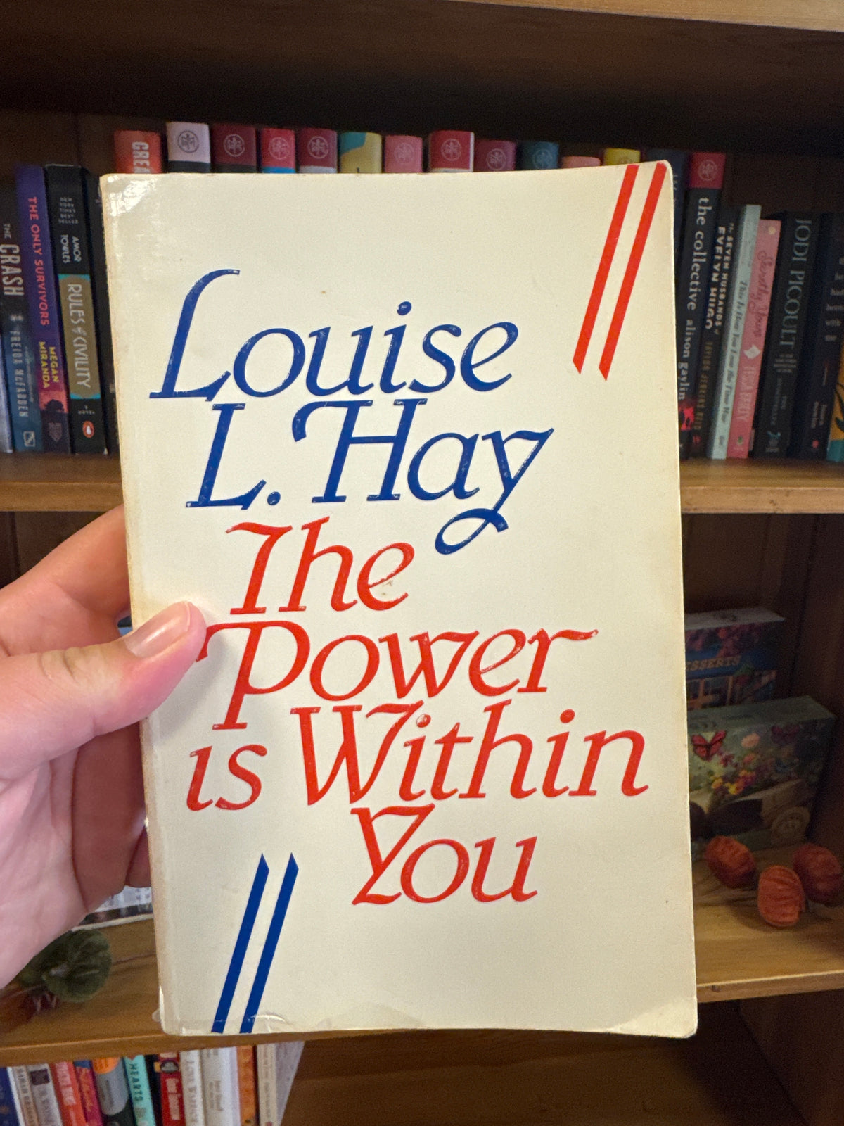The Power is Within You softcover book by Louise Hay on wooden bookshelf