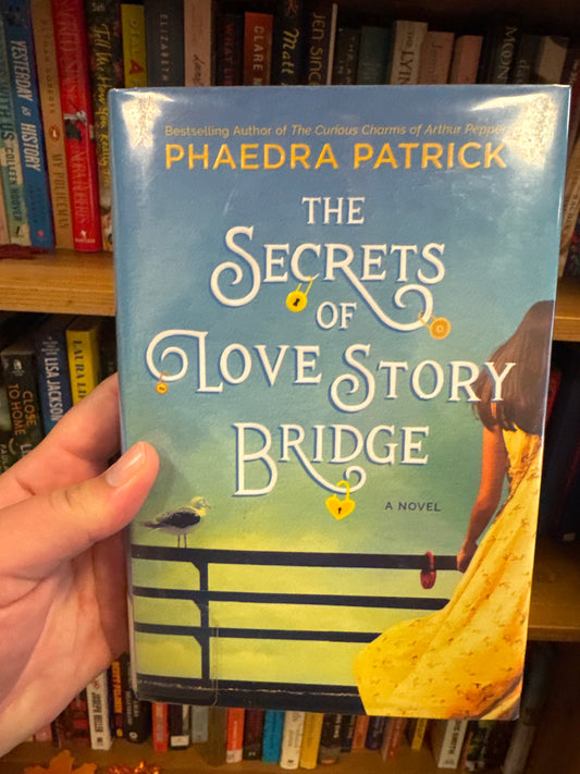 The Secrets of Love Story Bridge hardcover novel by Phaedra Patrick with blue sky cover art