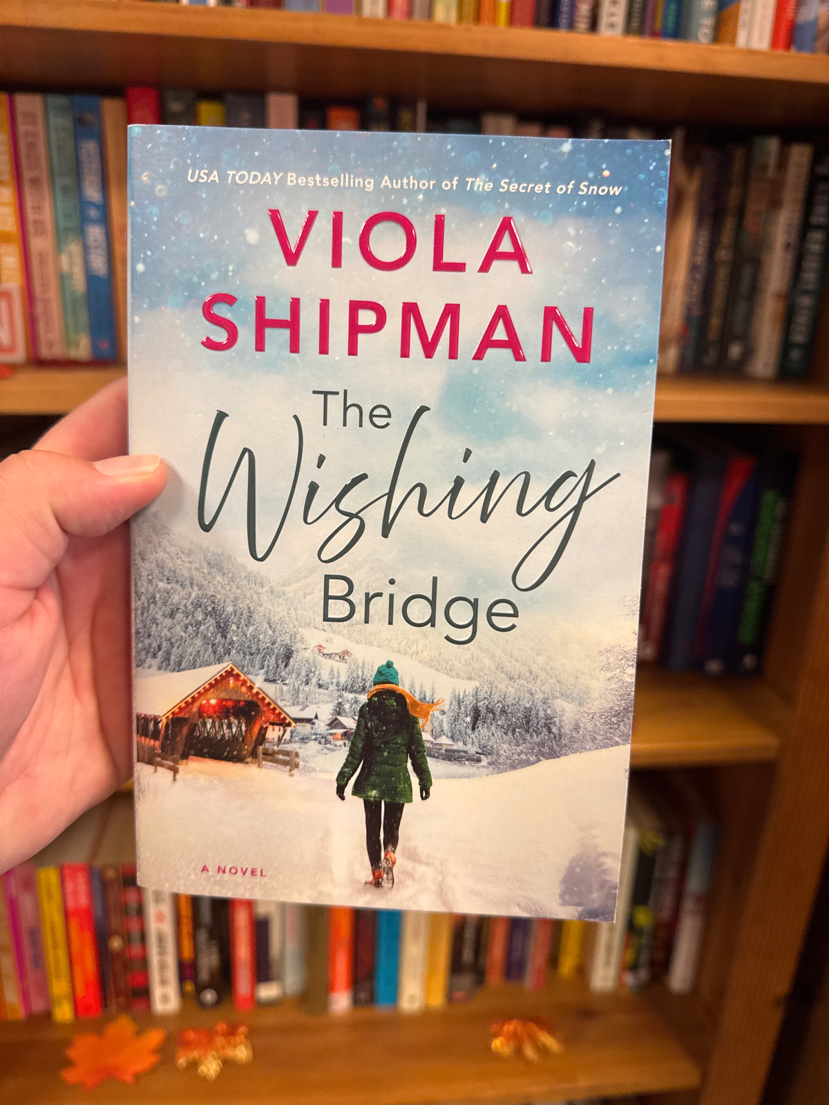 The Wishing Bridge paperback novel by Viola Shipman held in hand with snowy bridge cover art
